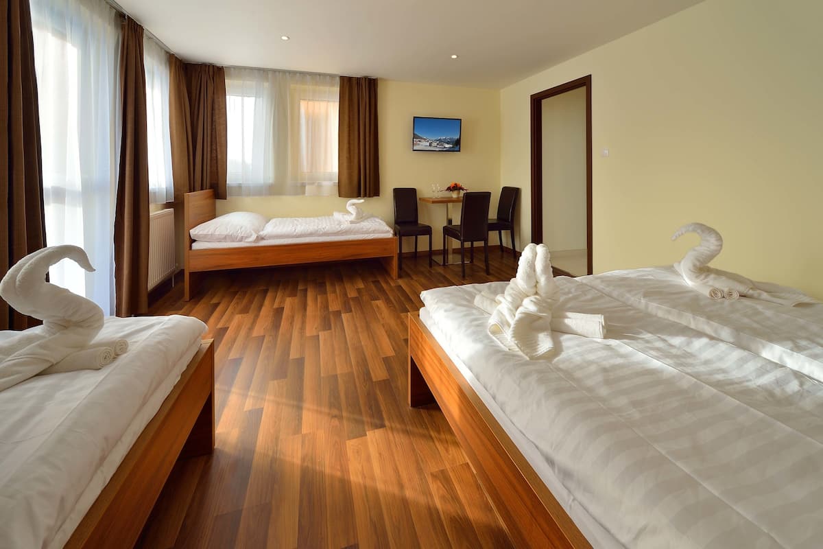 A hotel room with two beds, a wooden floor, a desk with chairs, and a TV on the wall.