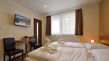 A hotel room with two beds, a TV mounted on the wall, a small table with a vase of flowers, and a chair.
