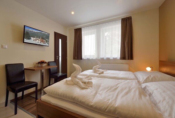 A hotel room with two beds, a TV mounted on the wall, a small table with a vase of flowers, and a chair. - Villa Gloria (Donovaly)
