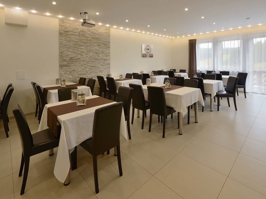 A dining area with multiple tables and chairs, a stone accent wall, and large windows with curtains.