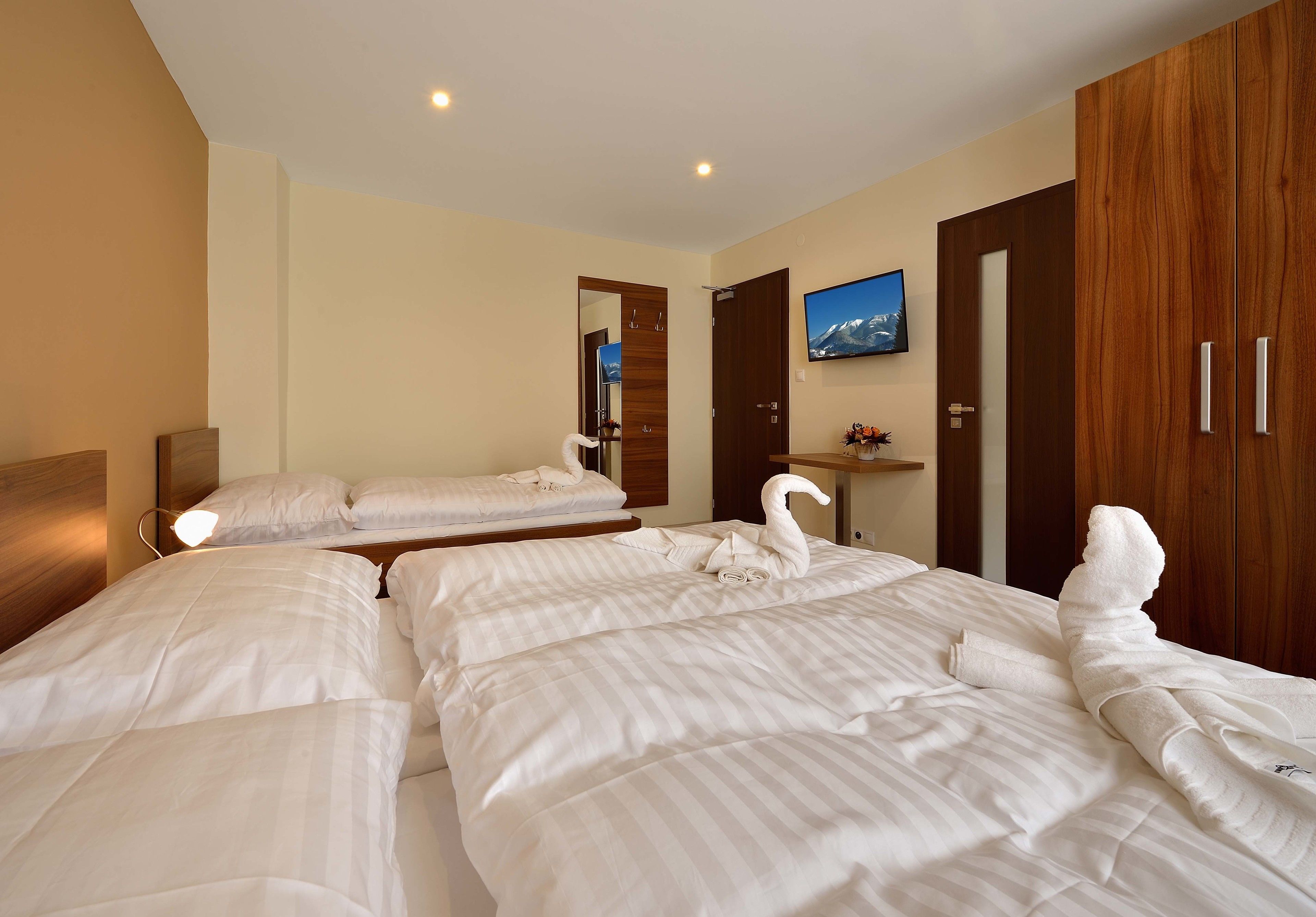 A hotel room with two beds, a TV mounted on the wall, and wooden wardrobes.