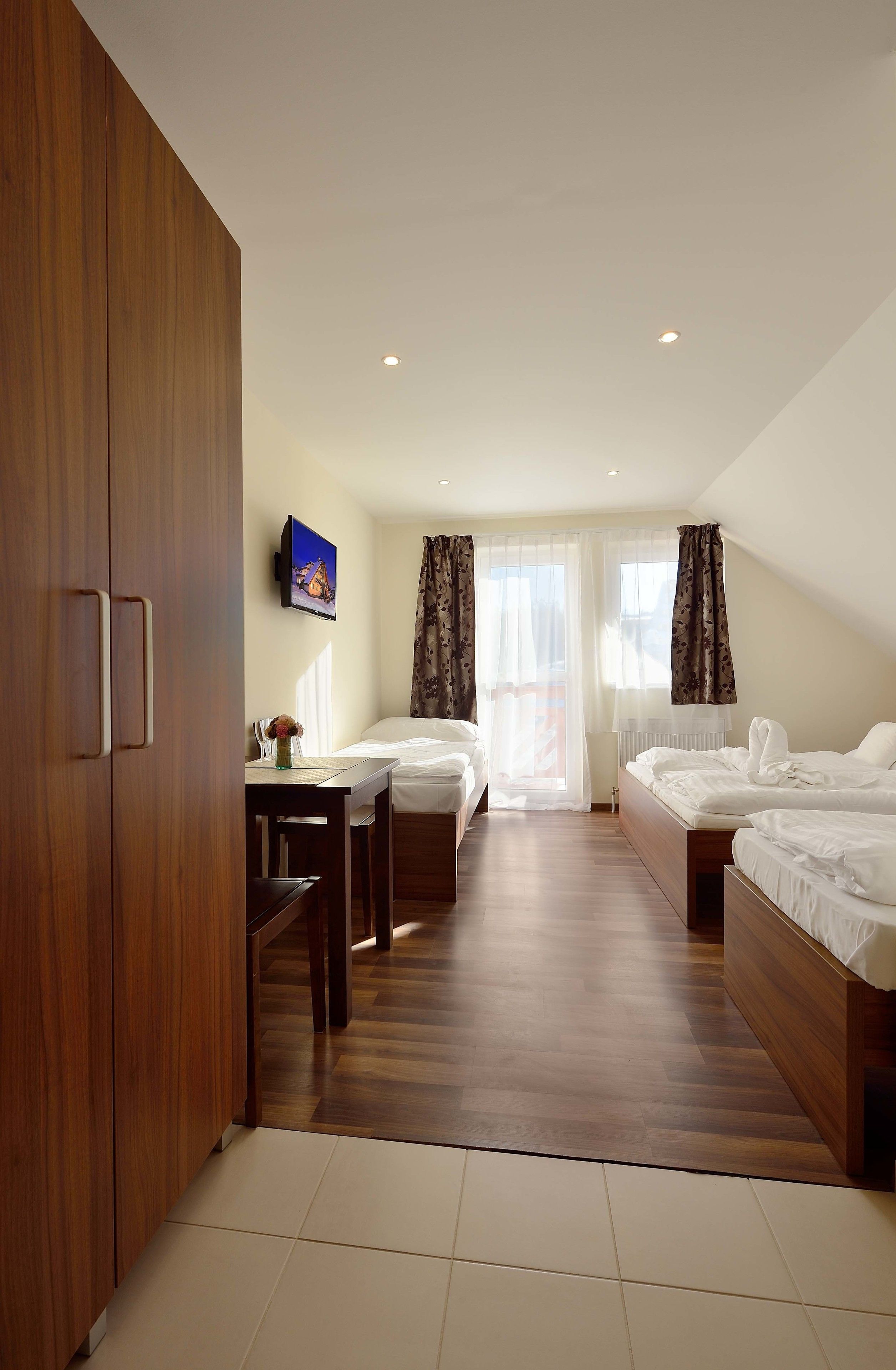 Habitación de hotel con dos camas, un armario de madera, un escritorio y un televisor en la pared.