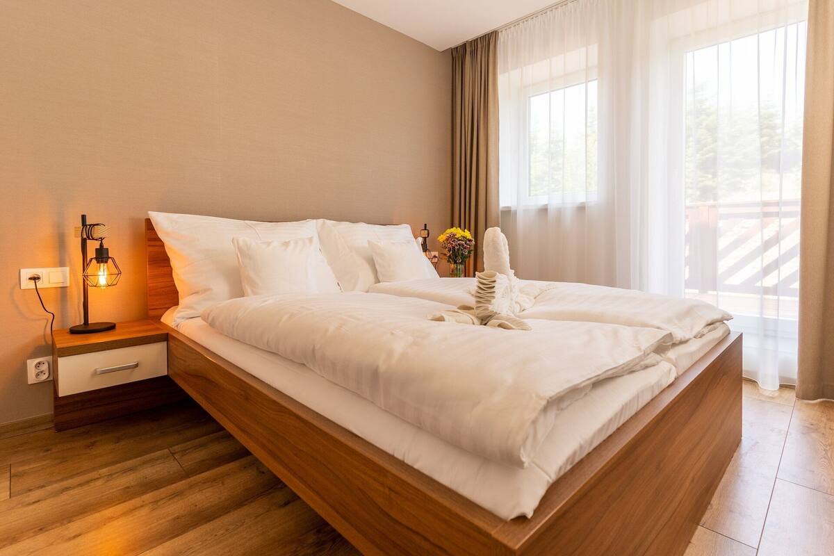 A neatly made bed with white linens, a bedside lamp, and a vase with flowers.