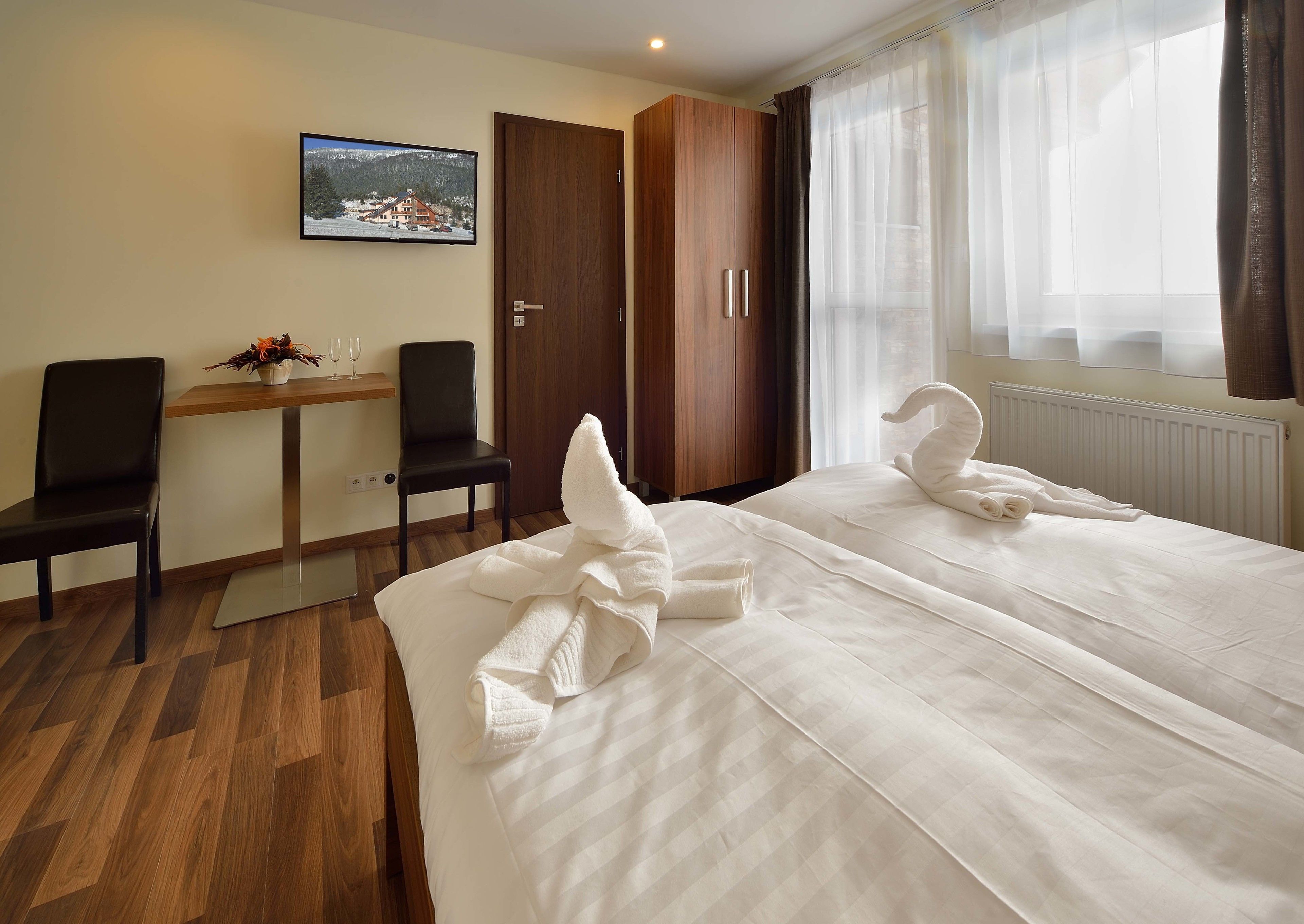 A hotel room with two beds, a wooden desk, a chair, a television, and a window with curtains.