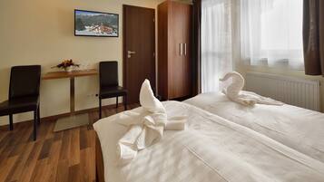 A hotel room with two beds, a wooden desk, a chair, a television, and a window with curtains.
