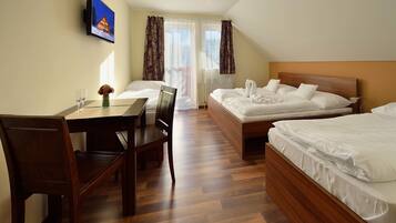 Habitación de hotel con dos camas individuales, un escritorio de madera con sillas, un televisor montado en la pared y una ventana con cortinas.