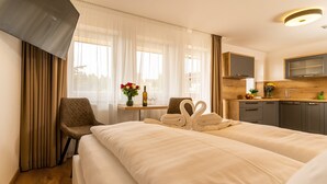 Habitación de hotel con cama, una silla, una mesita con un florero y una kitchenette.