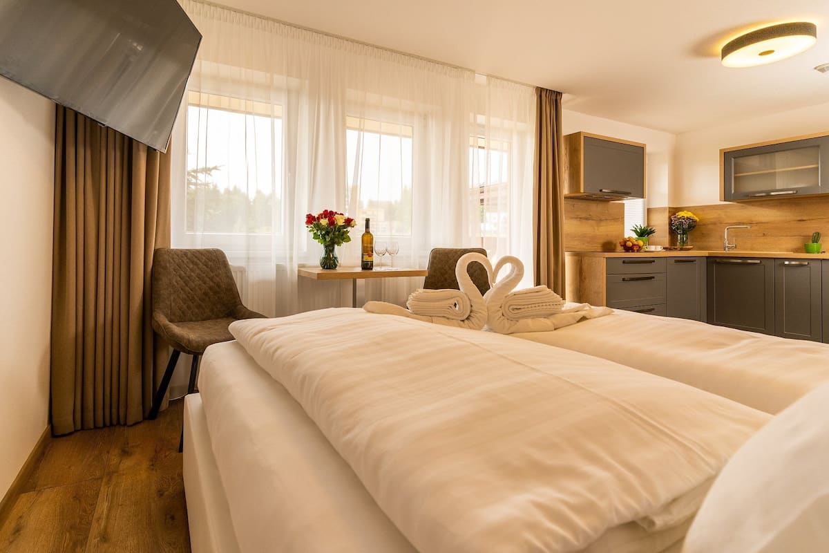 A hotel room with a bed, a chair, a small table with a vase of flowers, and a kitchenette.