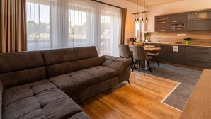 Una sala moderna con un sofá modular, un comedor con sillas, una cocina con armarios grises y un ventanal con cortinas translúcidas.