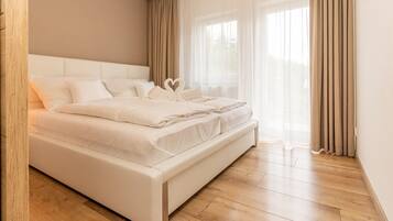 A modern bedroom with a large bed, wooden flooring, and sheer curtains.