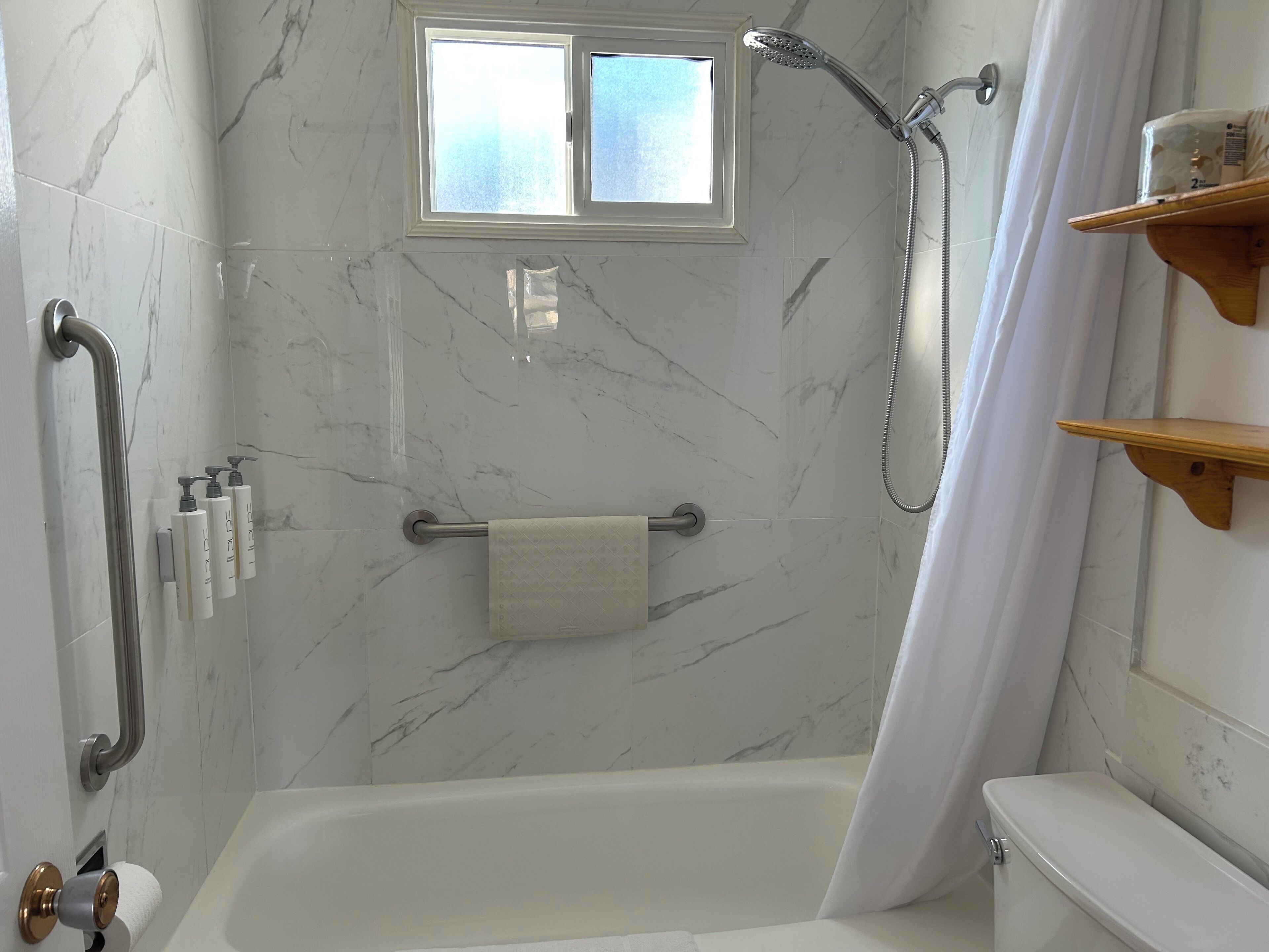 Un baño con bañera, ducha, paredes de mármol, una ventana y un inodoro.