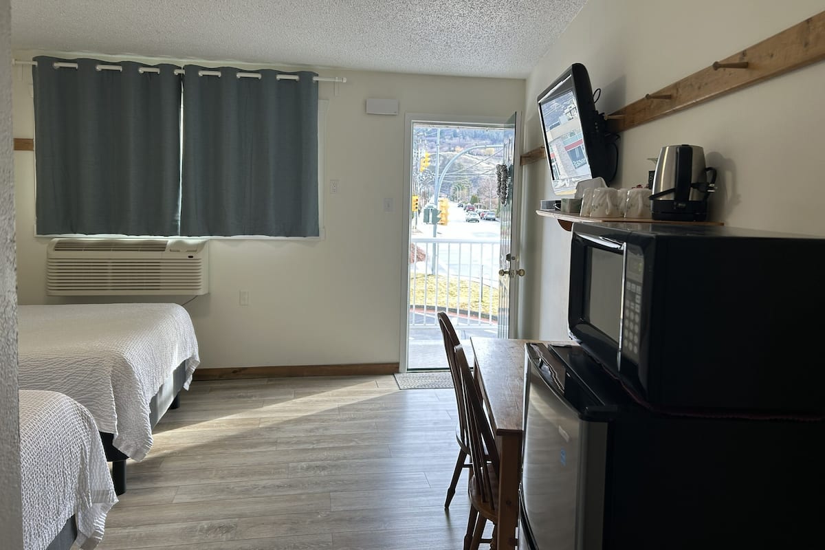 Habitación de hotel con dos camas, televisor, cafetera y vista a la calle desde la puerta.
