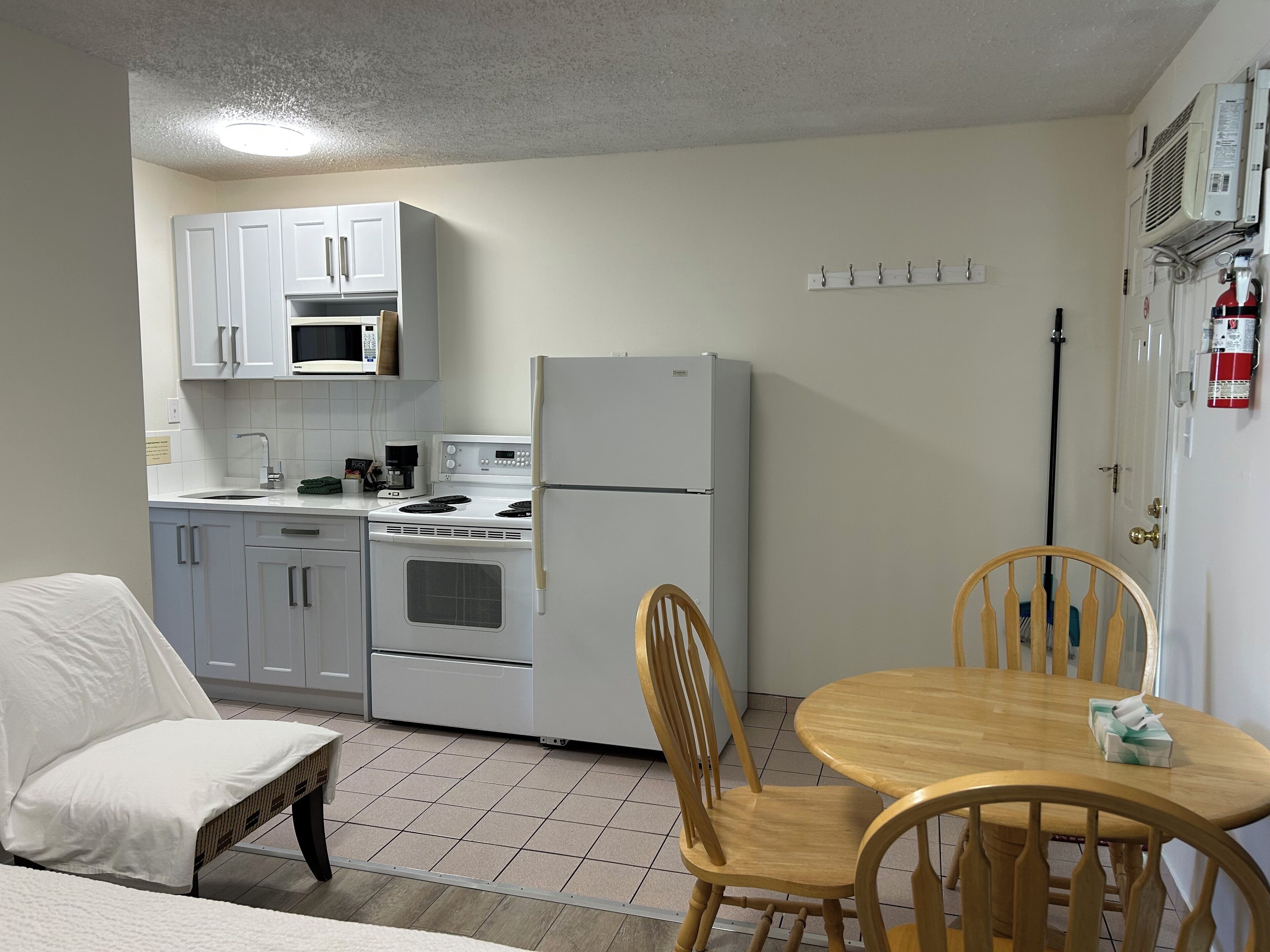 A compact kitchen with white cabinets, a microwave, a stove, and a refrigerator. There is a dining table with two chairs.