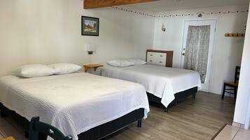 A room with two beds, a wooden ceiling, a small table, a chair, a picture on the wall, and a door with curtains.