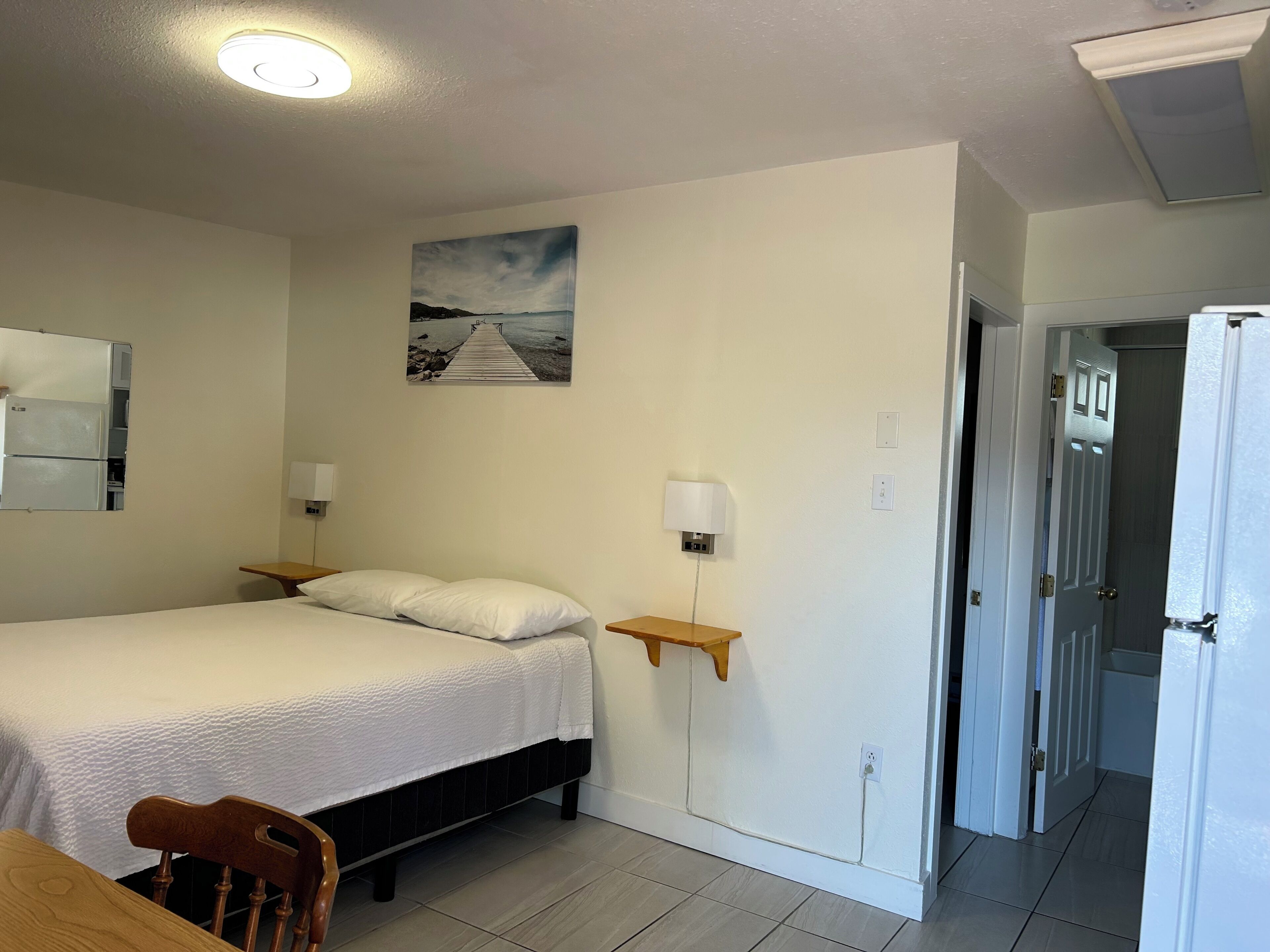 Een hotelkamer met een bed, nachtkastjes, een lamp, een schilderij en een deur naar een badkamer.