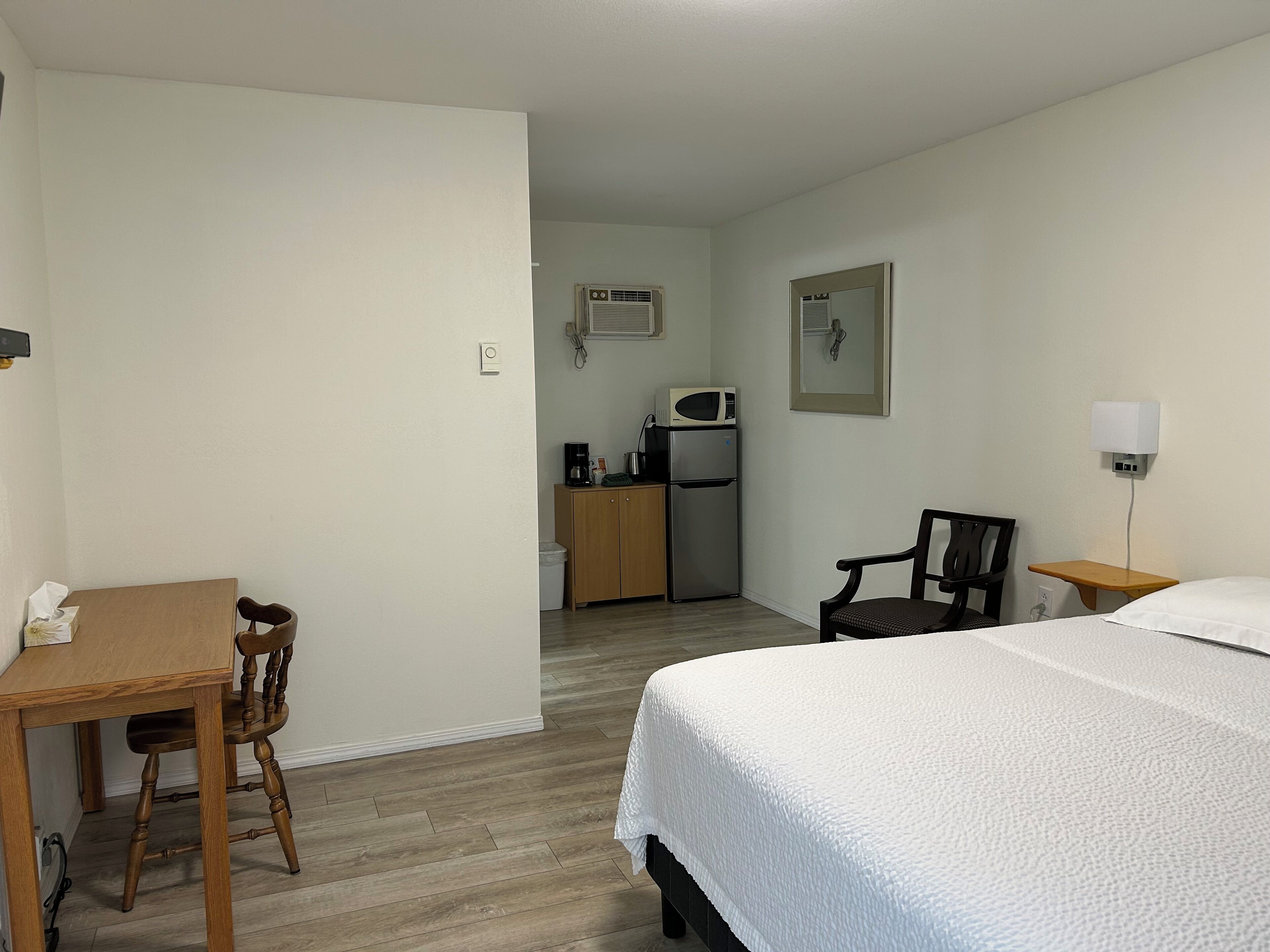 A hotel room with a bed, a desk, a chair, a kitchenette, and a small table.