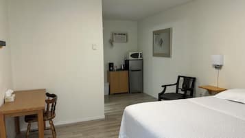 A hotel room with a bed, a desk, a chair, a kitchenette, and a small table.