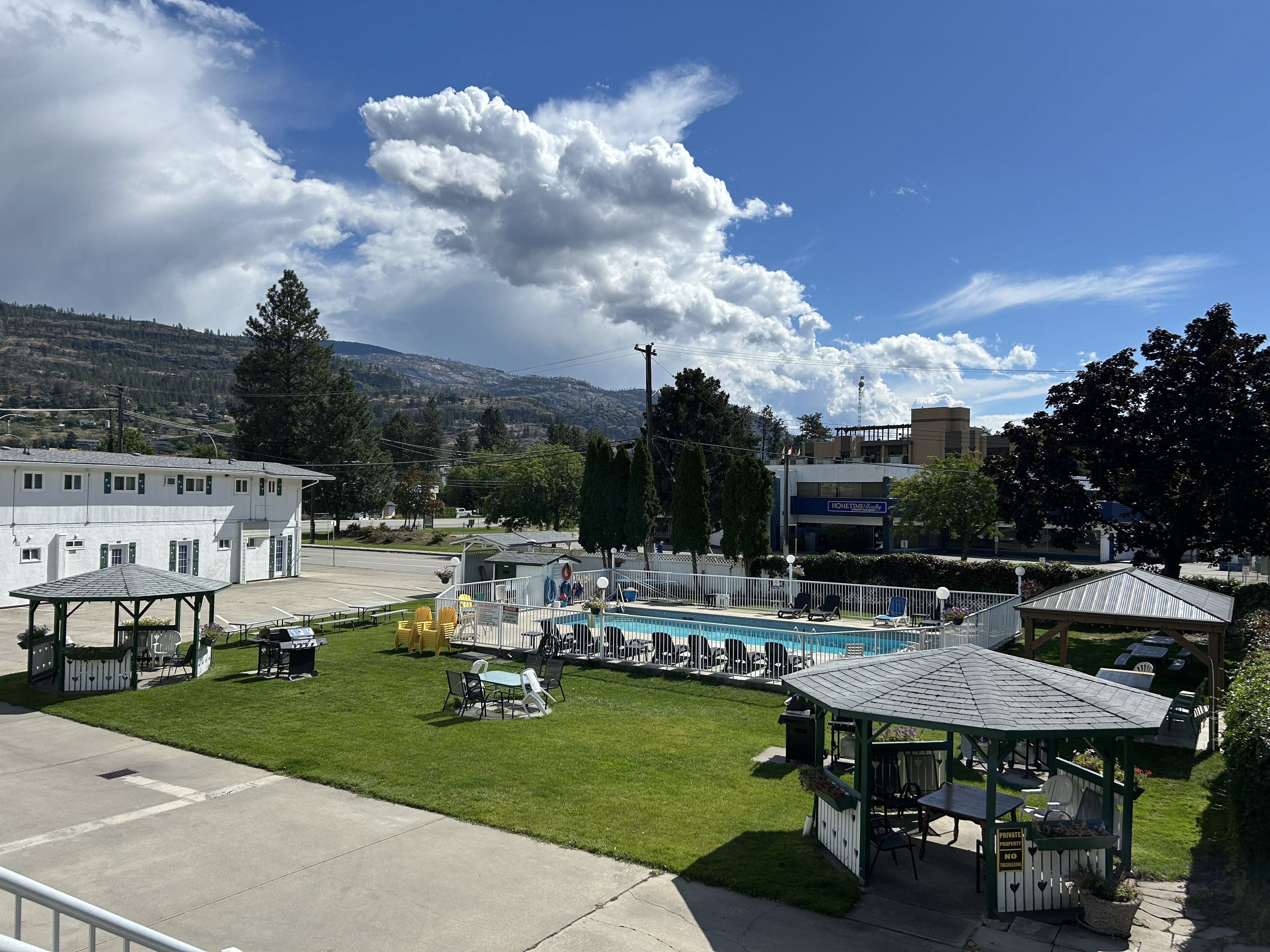 A pool area with lounge chairs and a gazebo, surrounded by a well-maintained lawn and a parking lot.
