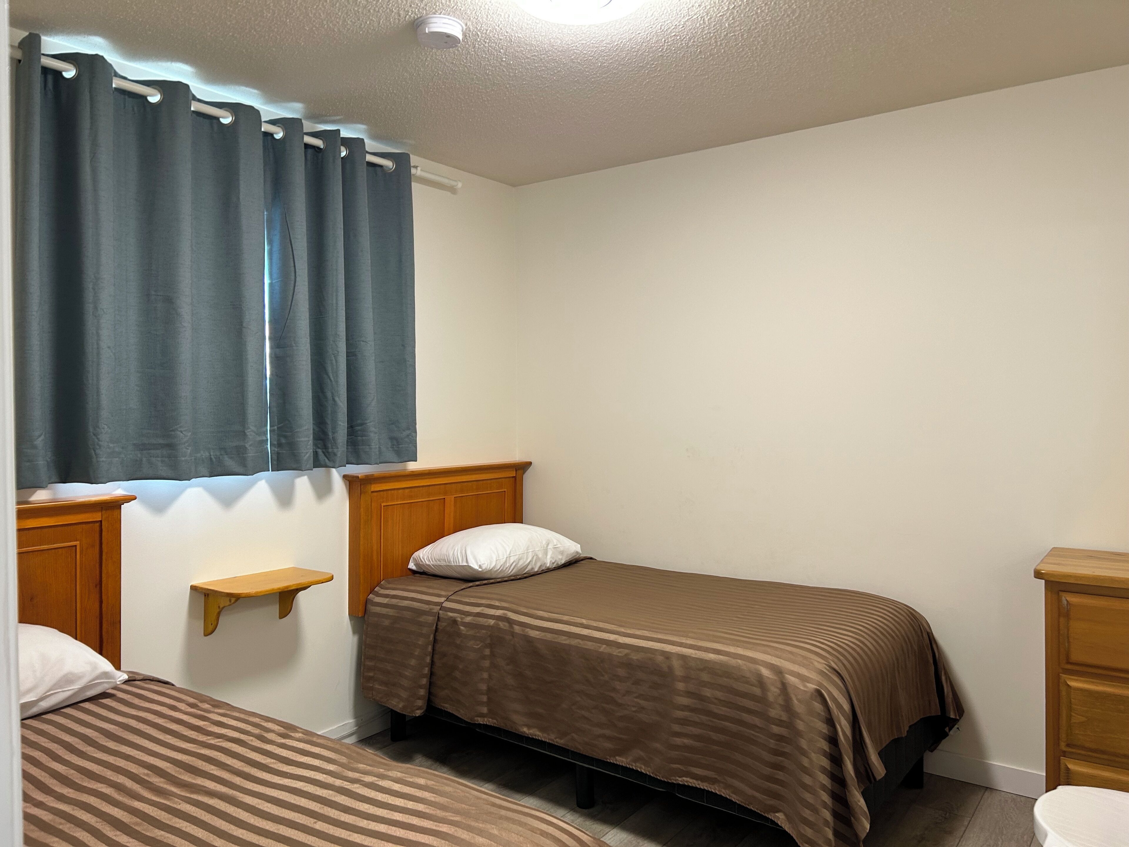 A small, single-bed room with a wooden headboard, a bedside table, and a window with curtains.