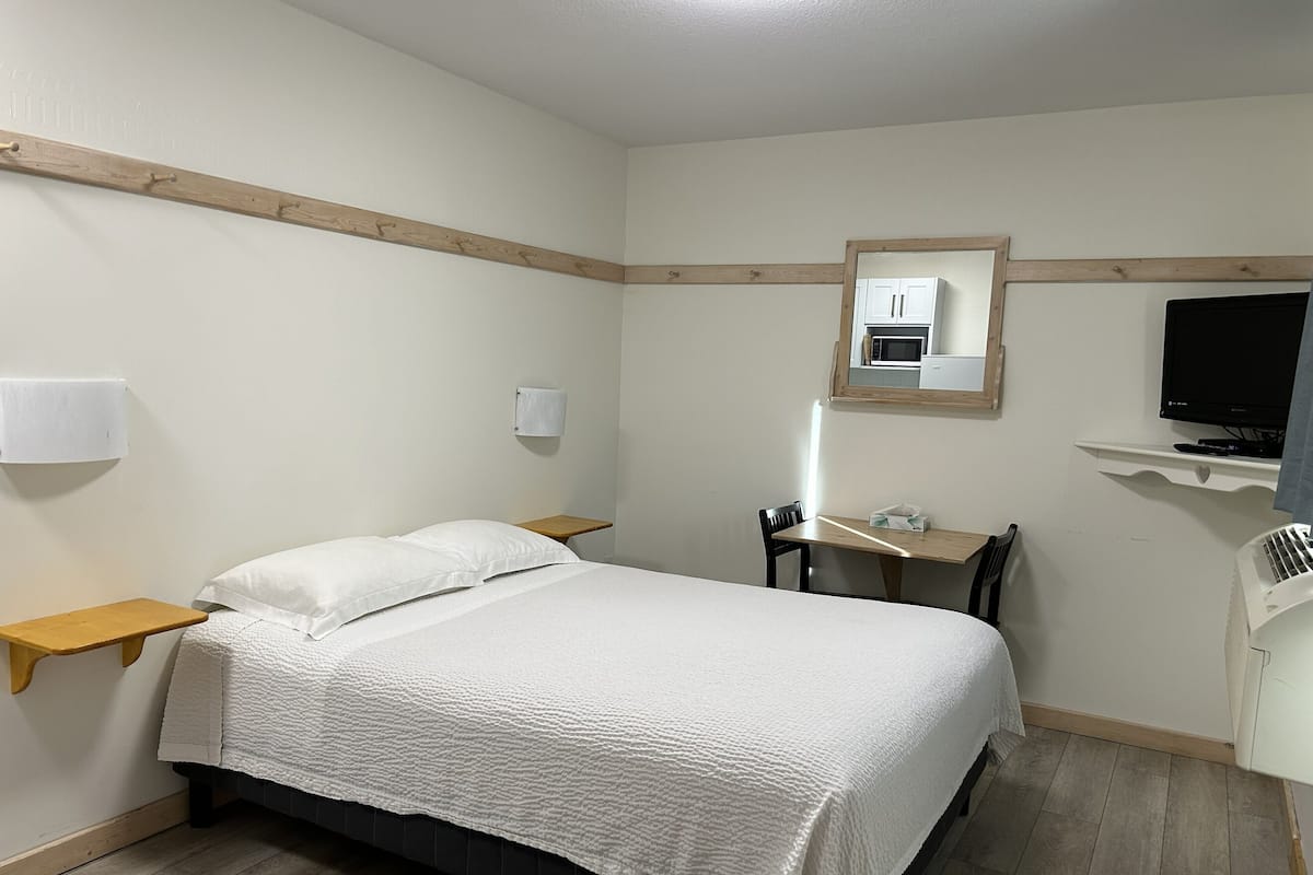 Un dormitorio con cama, mesitas de noche, escritorio, silla, televisor y microondas.