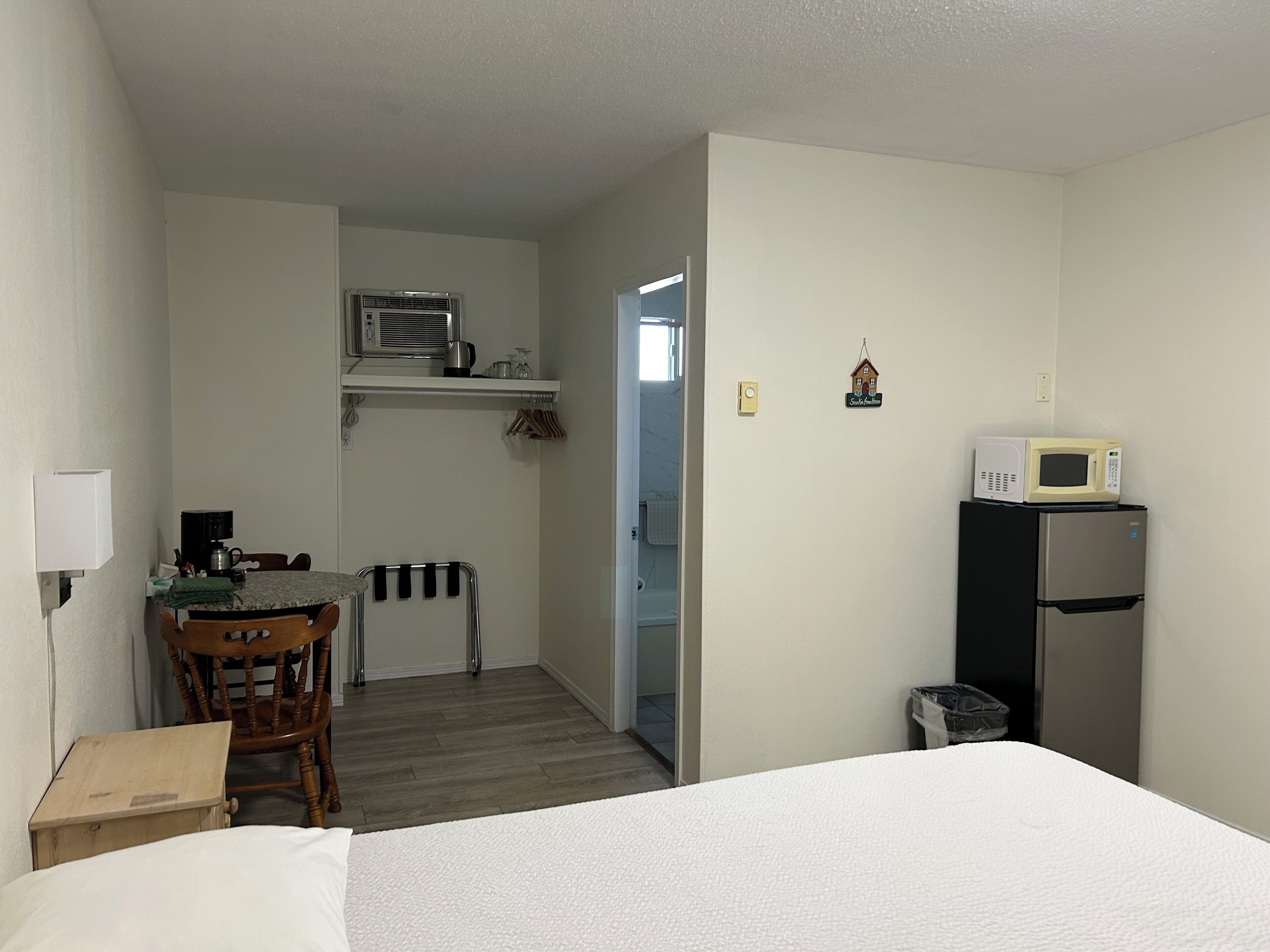 A hotel room with a bed, a wooden chair, a small table, a microwave, and a refrigerator.