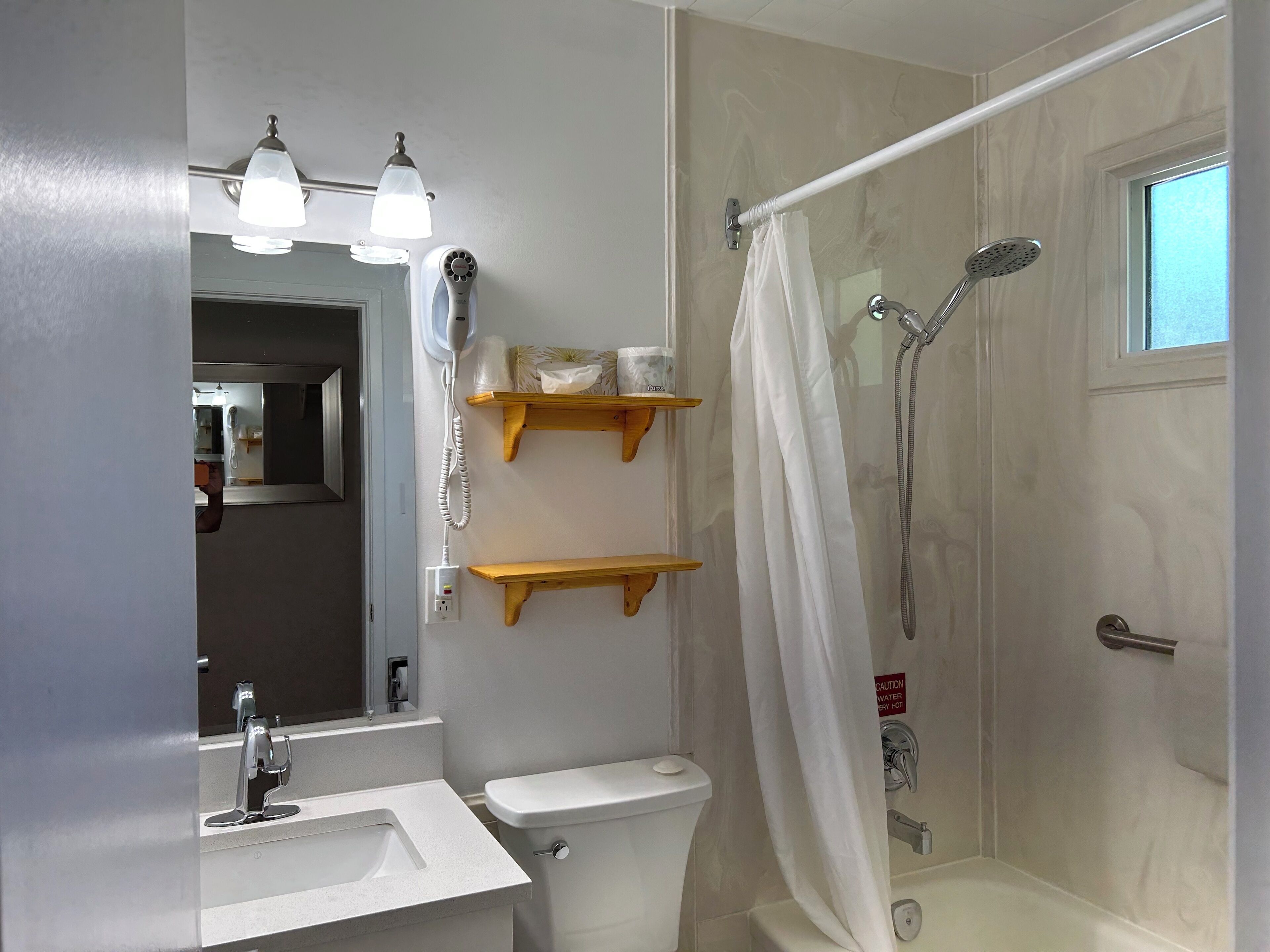 Un baño con inodoro, lavamanos, espejo, ducha y dos estantes de madera.