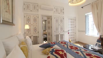 Un dormitorio con cama, almohadas, una mesita de noche y una ventana con cortinas.