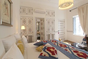 Quarto com cama, almofadas, mesa de cabeceira e janela com cortinas.