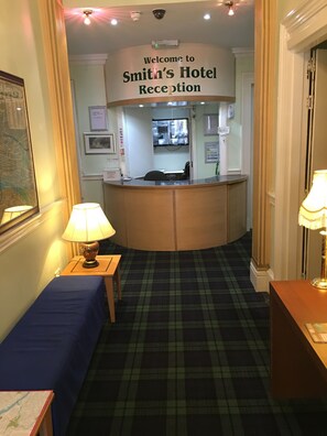 A reception area with a reception desk, a blue sofa, and a carpeted floor. - Smiths Hotel (Glasgow)