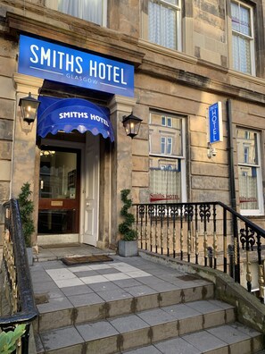 The exterior of the Smiths Hotel in Glasgow, featuring a prominent blue awning, a stone facade, and a staircase leading to the entrance. - Smiths Hotel (Glasgow)