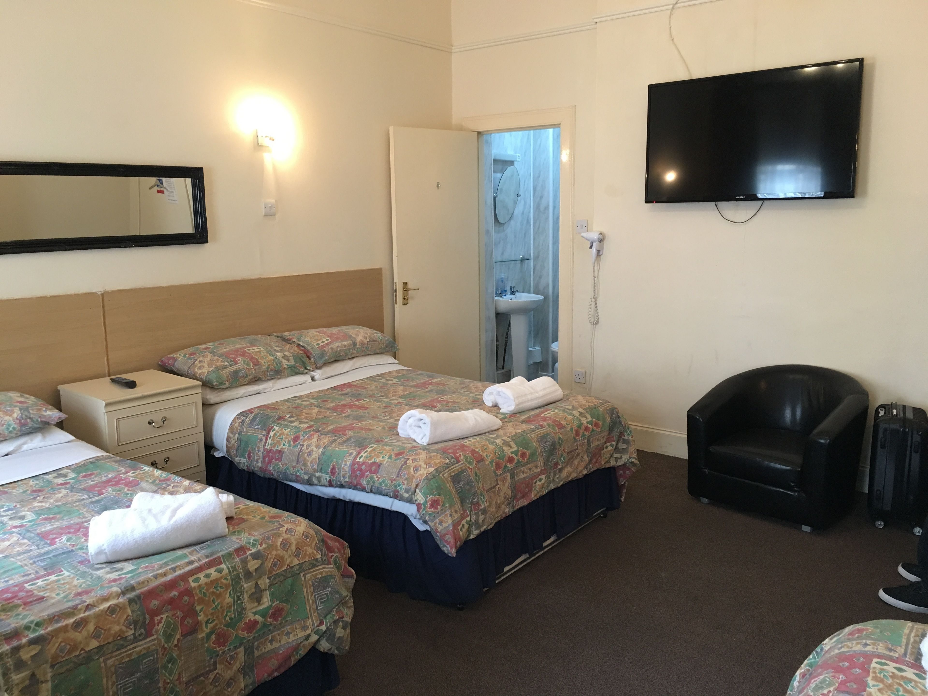 Habitación de hotel con dos camas, televisión, una silla y un baño visible a través de una puerta abierta.