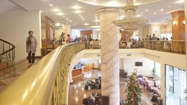 A hotel lobby with marble columns, a grand chandelier, and a Christmas tree.