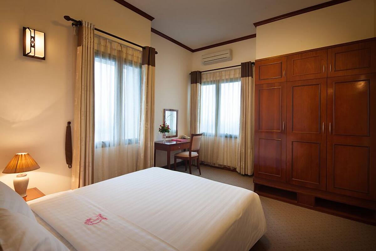 Quarto de hotel com uma cama grande, uma escrivaninha, uma cadeira e um guarda-roupa.