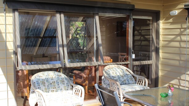 A covered patio with wicker chairs and a glass table, large windows, and a view of the outdoors.