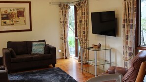A living room with a brown sofa, a glass coffee table, a flat-screen TV, and patterned curtains.