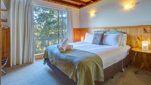 Un dormitorio con una cama grande, una mesita de noche, una ventana con cortinas y vistas a árboles.