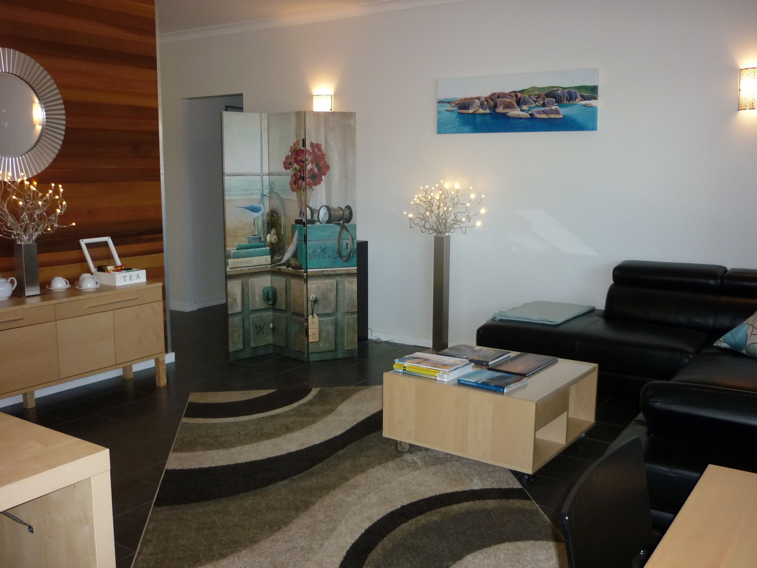 Un salon moderne avec un meuble en bois, un canapé en cuir noir, une table basse et un tableau accroché au mur.
