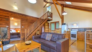 Una sala de estar acogedora con una escalera de madera, un sofá, una mesa de comedor y una zona de cocina con estufa y refrigerador.