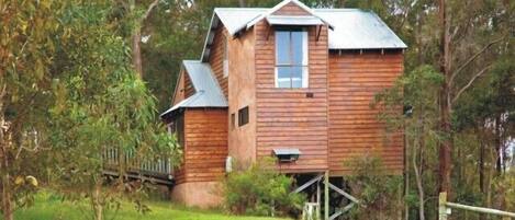 A wooden cabin with a gabled roof, a front porch, and a small deck area.