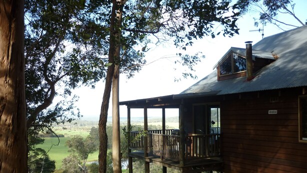 Una cabaña de madera con terraza, rodeada de árboles y vistas a un paisaje verde.