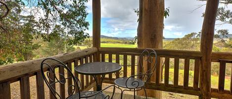 A wooden deck with two metal tables and chairs, overlooking a grassy landscape with trees and hills.