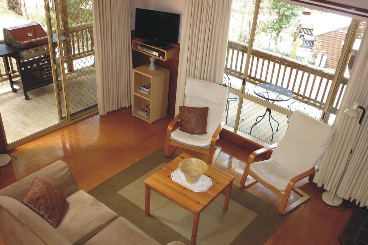 Uma sala de estar com sofá, duas poltronas, mesa de centro, televisão e estante de livros.