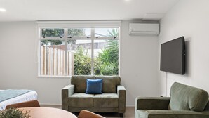 Una sala de estar moderna con un sofá, un televisor montado en la pared y un ventanal con vistas a un jardín.