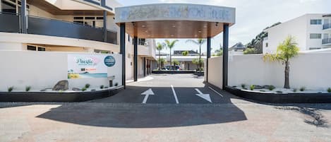 L’entrée d’un motel, avec un passage couvert, des flèches indiquant la direction et une enseigne « Pacific Motor Inn ».