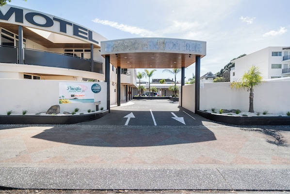 Entrada de um motel com galeria coberta, setas de direção e placa Pacific Motor Inn.