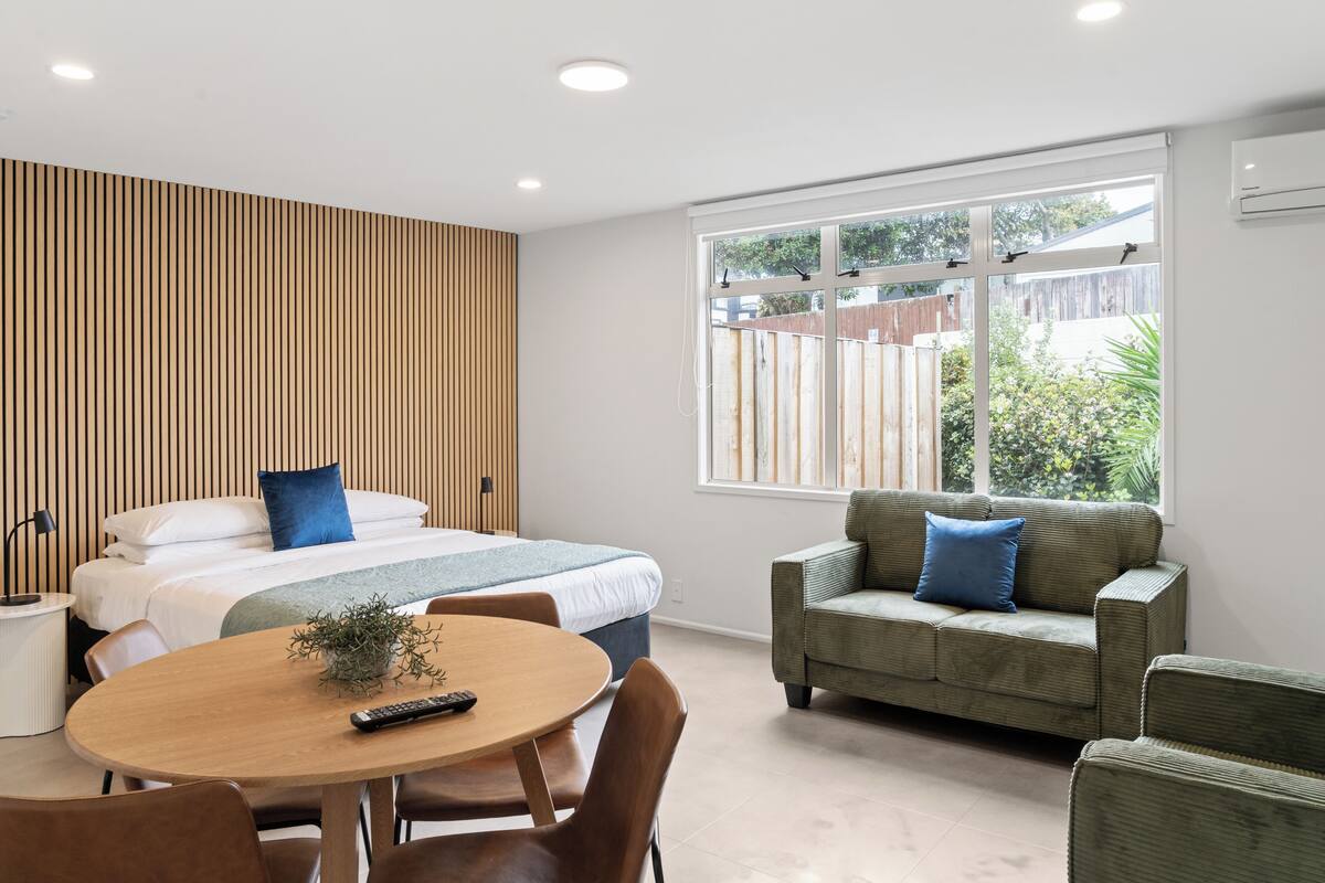 Ein modernes Hotelzimmer mit einem großen Bett, einem grünen Sofa, einem Esstisch und einem Fenster mit Blick nach draußen.