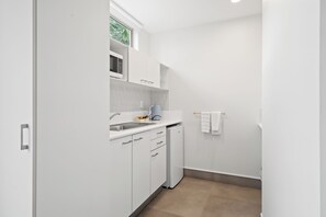 Une cuisine compacte avec des meubles blancs, un four à micro-ondes, un évier et un petit réfrigérateur.