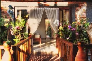 A wooden deck with a view of a room through sheer curtains, surrounded by potted plants and flowers. - Ngeluwungan Boutique Villa (Pererenan)
