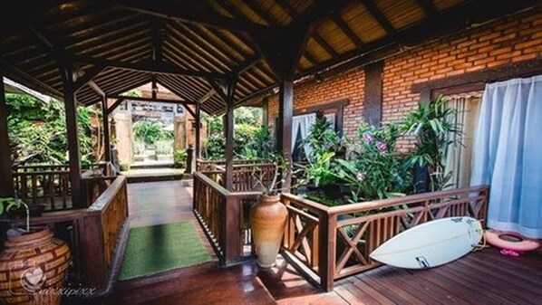 Una terraza cubierta de madera con un muro de ladrillo, una planta en maceta y una tabla de surf.