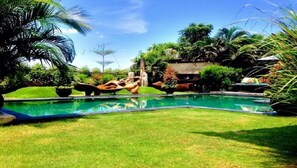 Une piscine entourée d’une végétation luxuriante, avec une structure en pierre en arrière-plan.